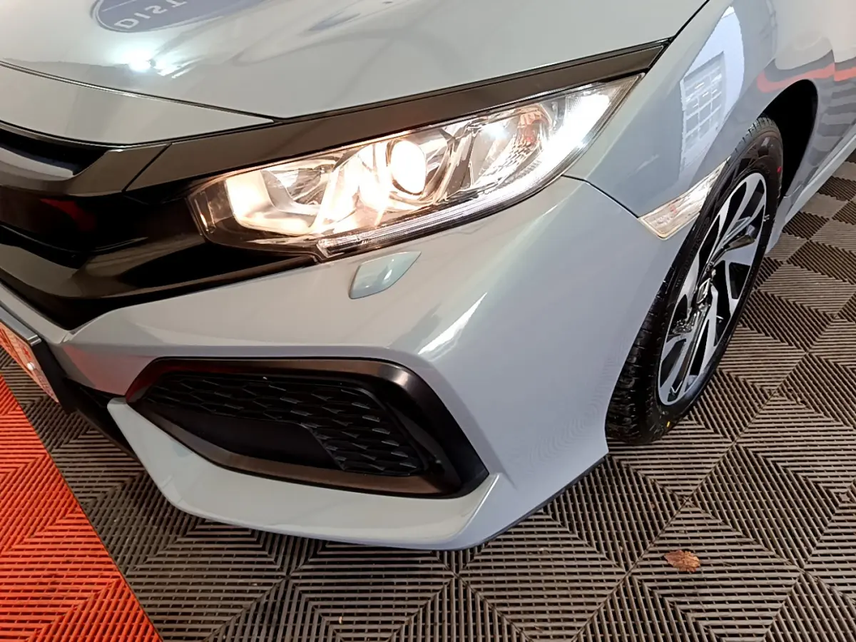 Gros plan sur l'avant droit gris clair d'une Honda Civic 2020 avec phare allumé et jante alliage noire.