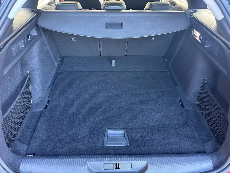 Coffre spacieux de la Peugeot 308 SW 2024 vu de l'arrière, avec tapis noir et filets de rangement latéraux.