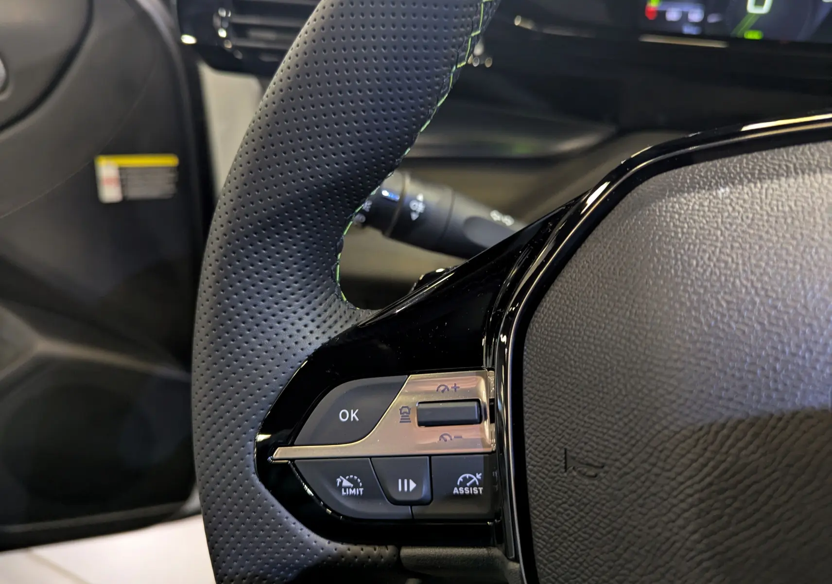 Gros plan sur la partie gauche du volant en cuir perforé noir de la Peugeot 308 GT 2025 avec commandes intégrées.