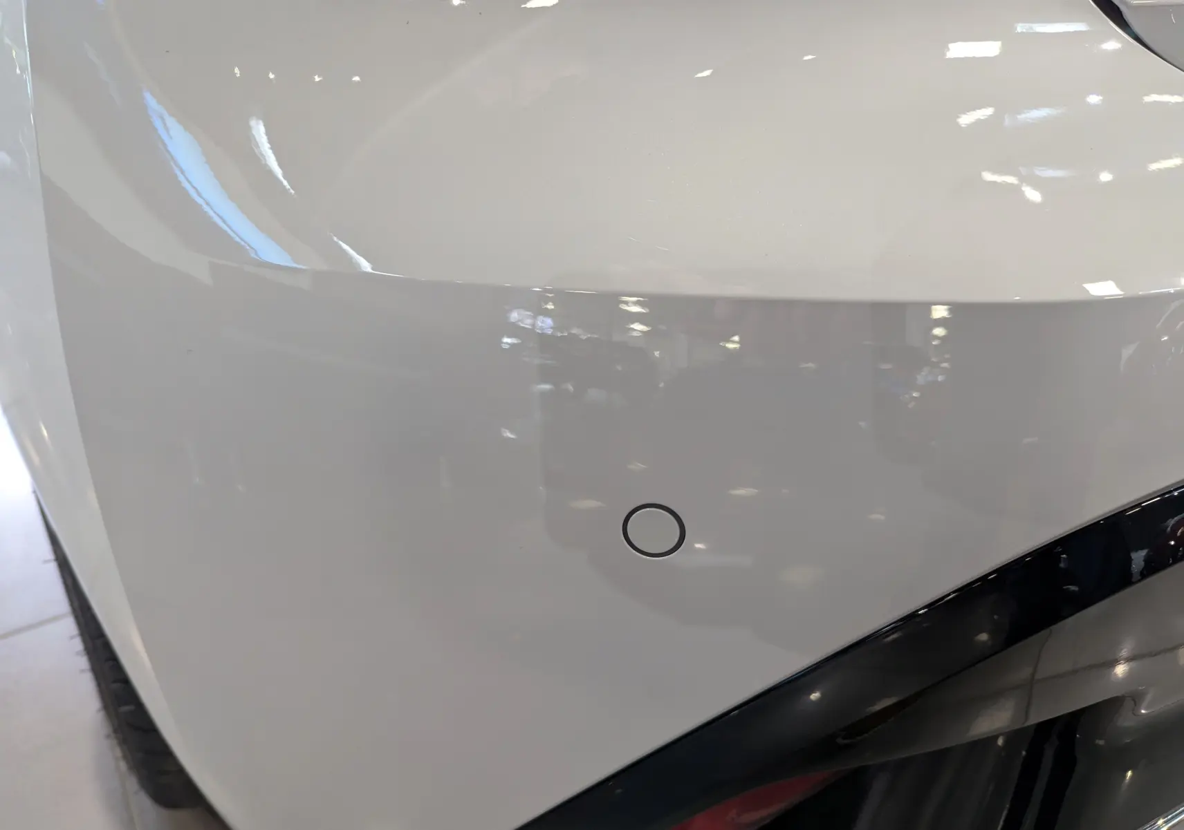 Détail du pare-chocs avant blanc Okénite d'une Peugeot 308 GT 2025 avec capteur de stationnement visible.