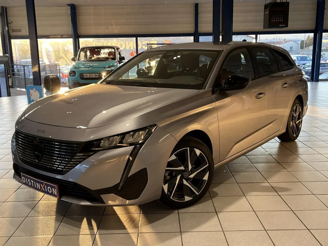Peugeot 308 SW gris clair métallisé vue 3/4 avant droit en showroom avec jantes alliage distinctives.