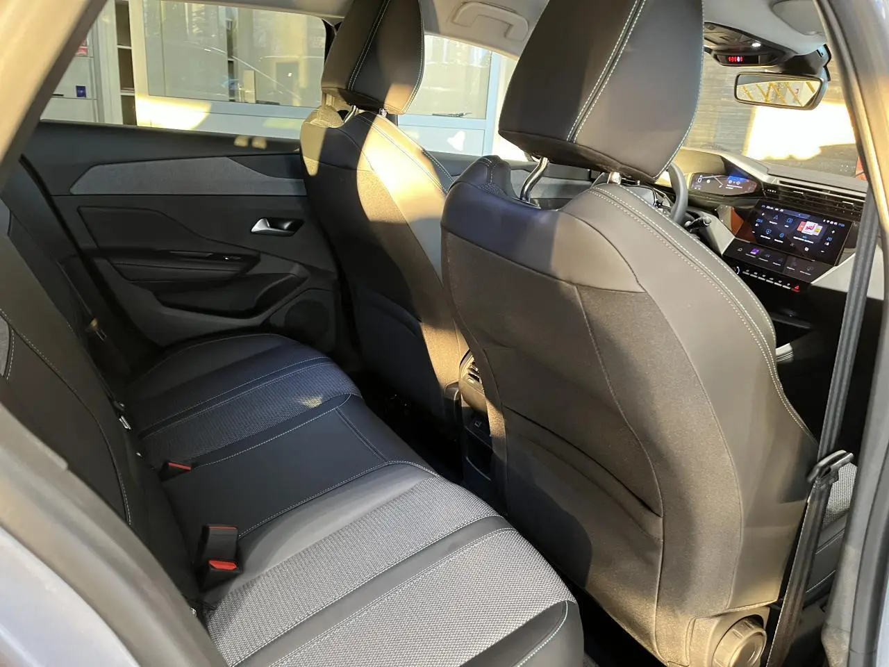 Intérieur arrière du Peugeot 308 SW 2024, vue côté gauche, sièges noirs avec surpiqûres blanches et tableau de bord numérique visible.