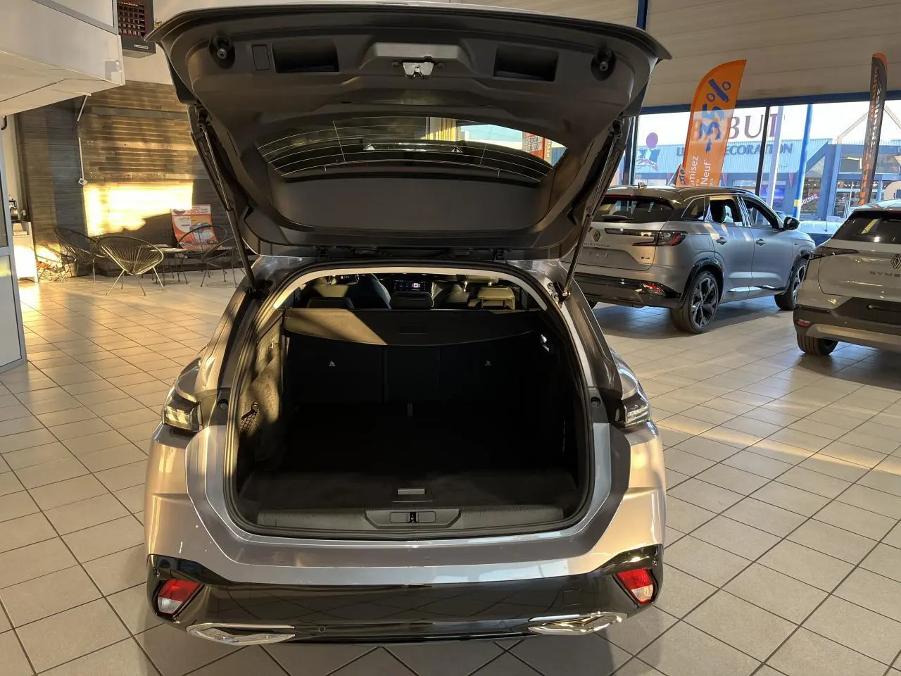 Vue arrière ouverte sur le coffre d'une Peugeot 308 SW 2024 gris clair Metal Artense en concession lumineuse.
