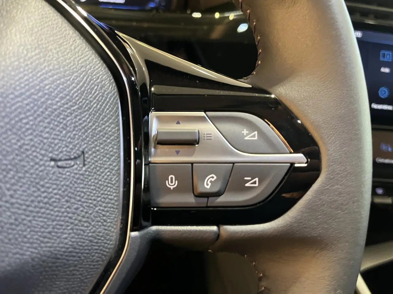 Gros plan sur les commandes du volant côté gauche du Peugeot 308 SW gris clair métal Artense 2024, version diesel.