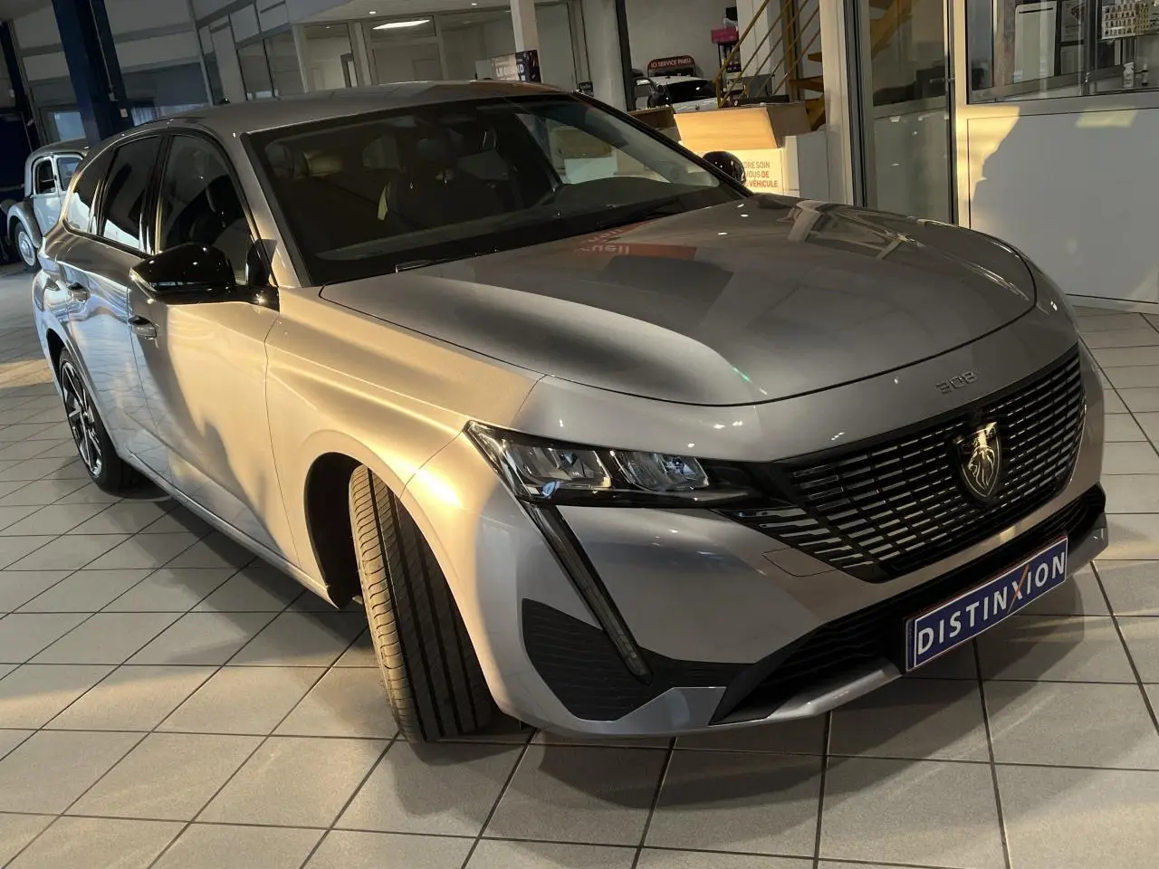 Peugeot 308 SW gris clair Metal Artense en 3/4 avant droit, avec calandre noire et feux LED distinctifs.