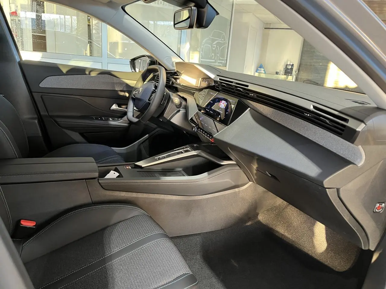 Intérieur côté conducteur de la Peugeot 308 SW 2024, avec tableau de bord moderne et sellerie noire textile.
