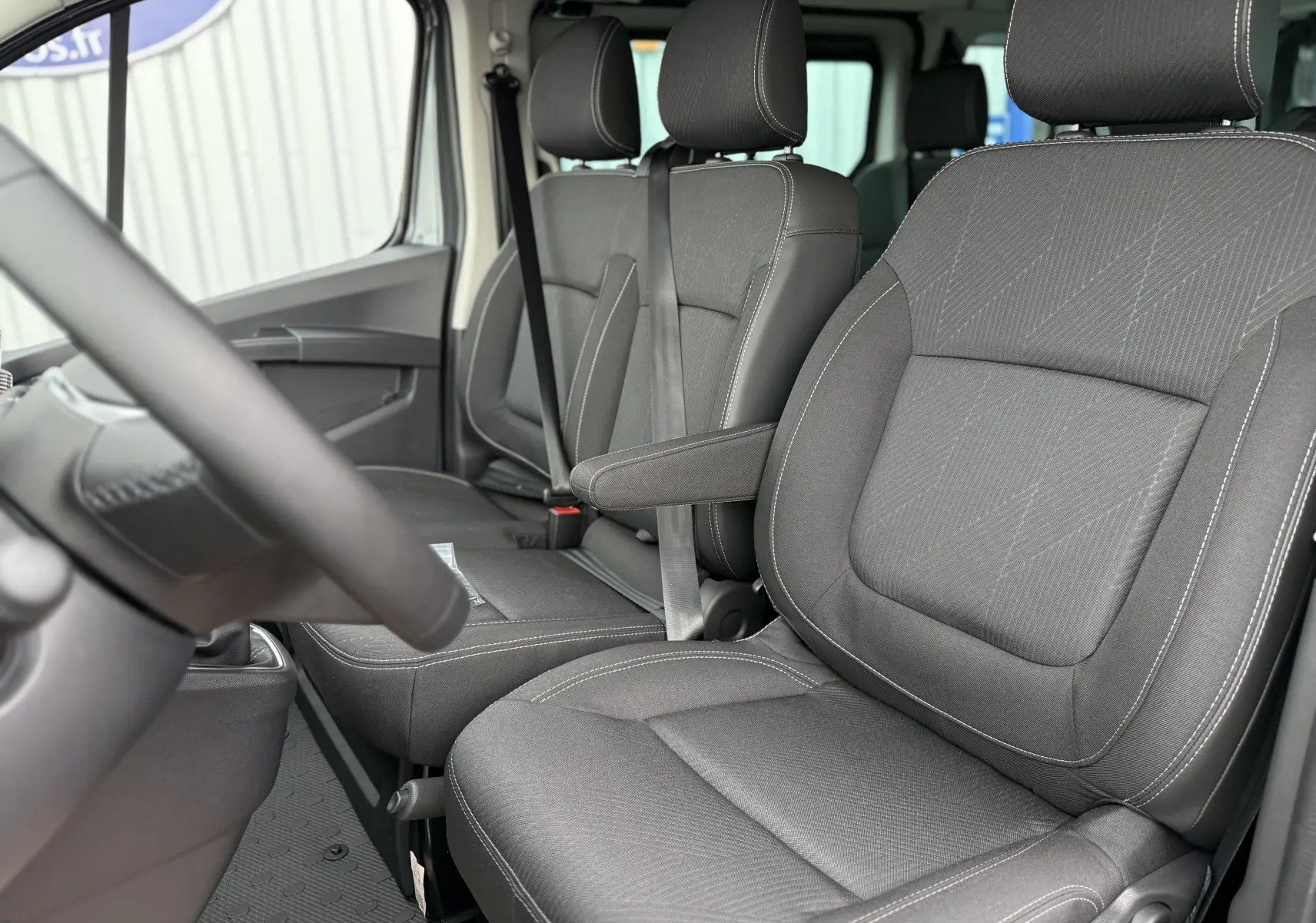 Intérieur du Renault Trafic Combi 2025, vue côté conducteur sur les sièges tissu gris urbain avec accoudoir central.