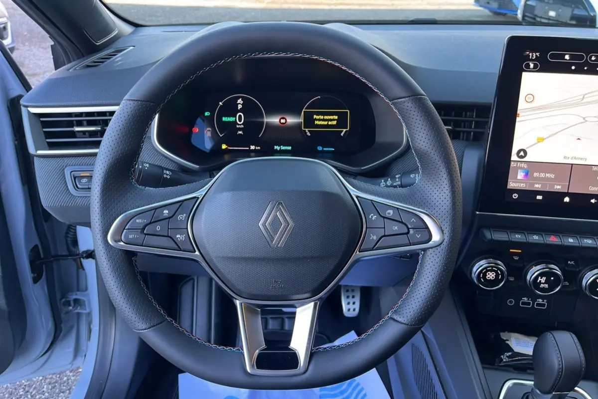 Vue intérieure centrée sur le volant cuir multifonctions et le tableau de bord digital de la Renault Clio V E-Tech 145 Esprit Alpine.