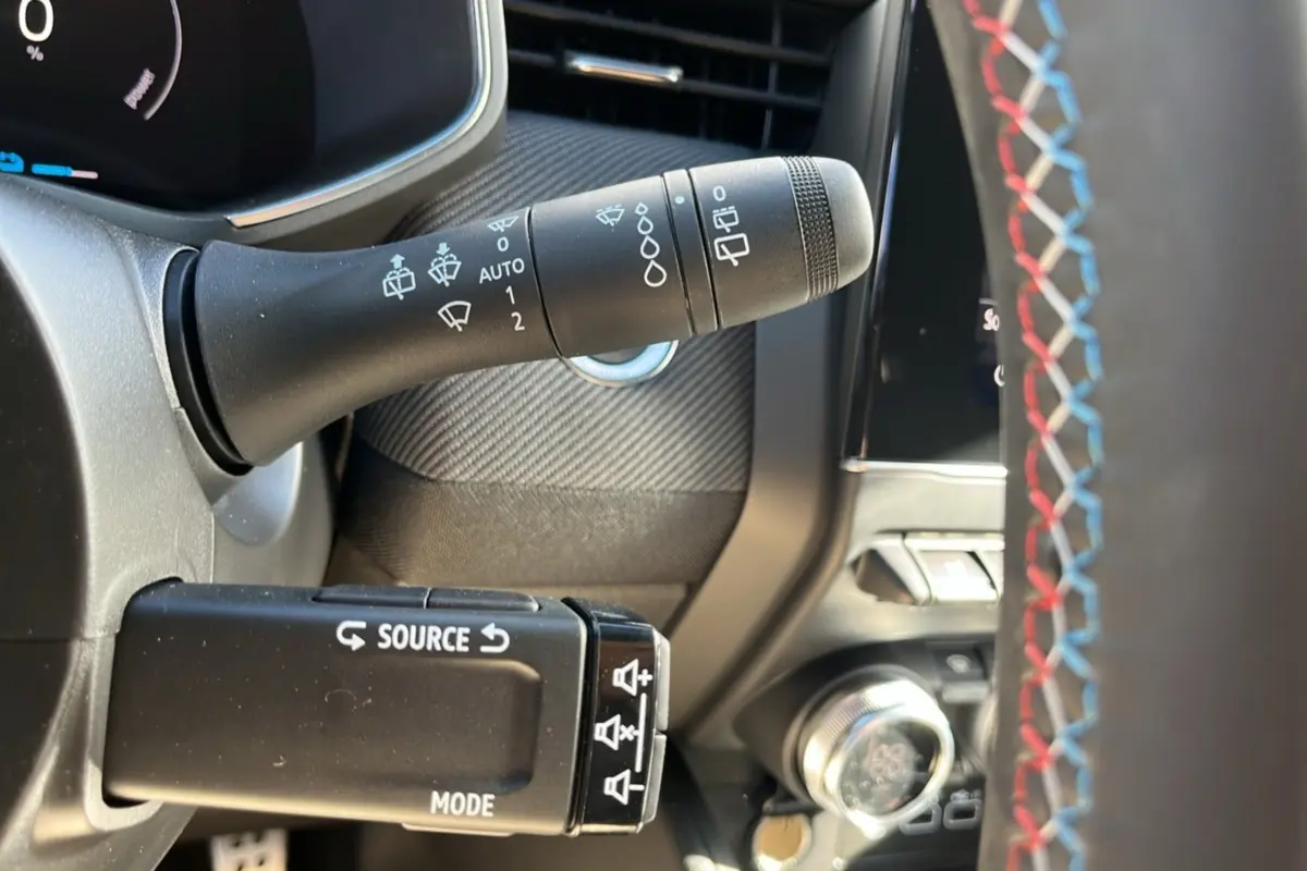 Gros plan sur la commande d’essuie-glace et la commande audio au volant avec surpiqûres tricolores du Renault Clio V E-Tech 145 Esprit Alpine.