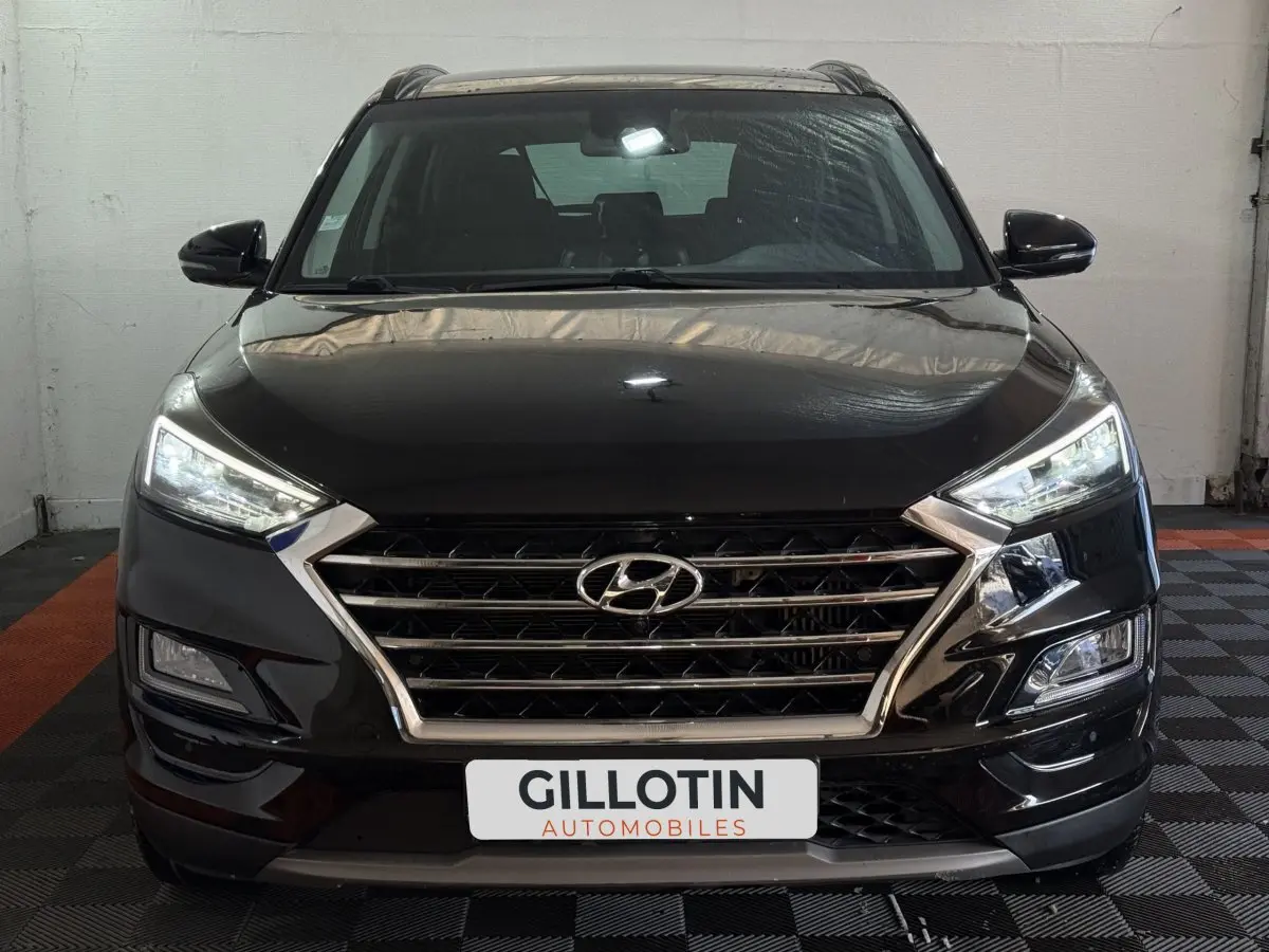 Vue frontale d'un Hyundai Tucson noir 2019 avec calandre chromée et phares LED allumés dans un garage.