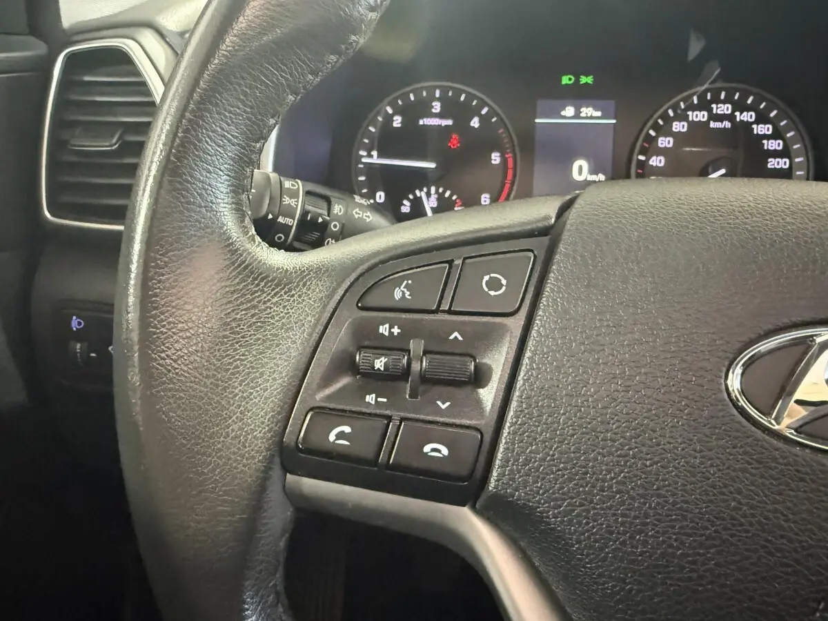 Gros plan sur le volant cuir noir du Hyundai Tucson 2019 avec commandes audio et tableau de bord éclairé.