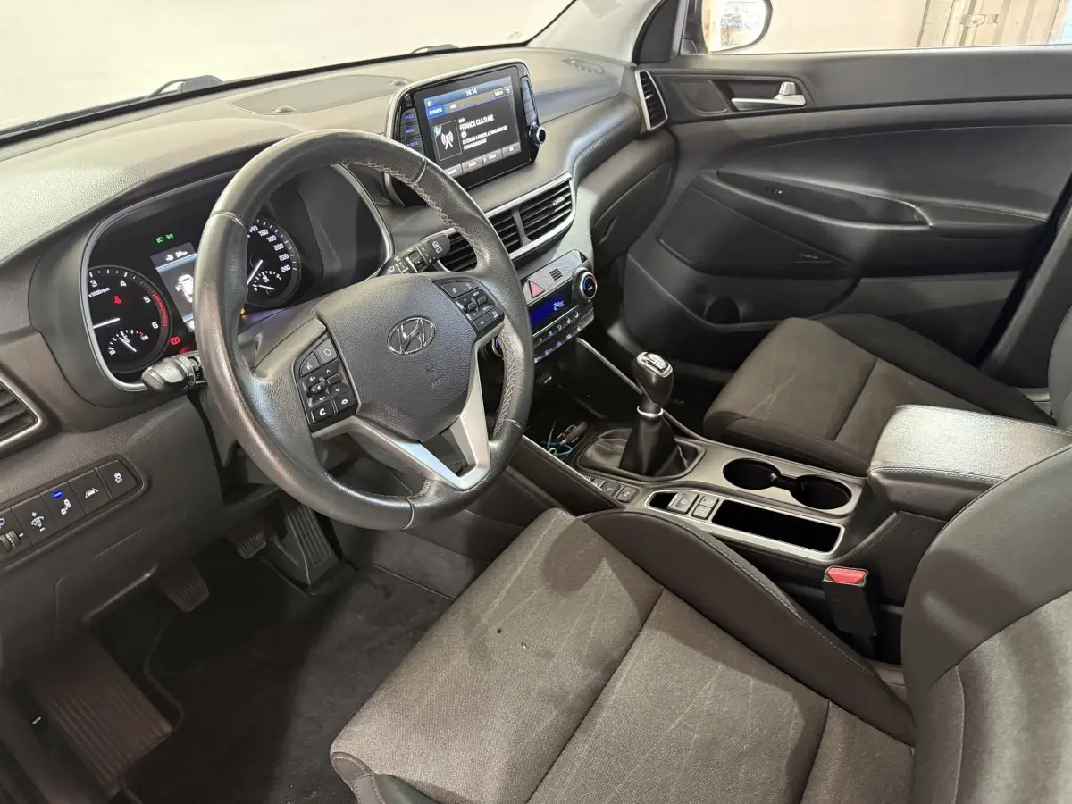 Vue intérieure côté conducteur du Hyundai Tucson 1.6 CRDI noir, volant cuir multifonctions et écran tactile 8 pouces visible.
