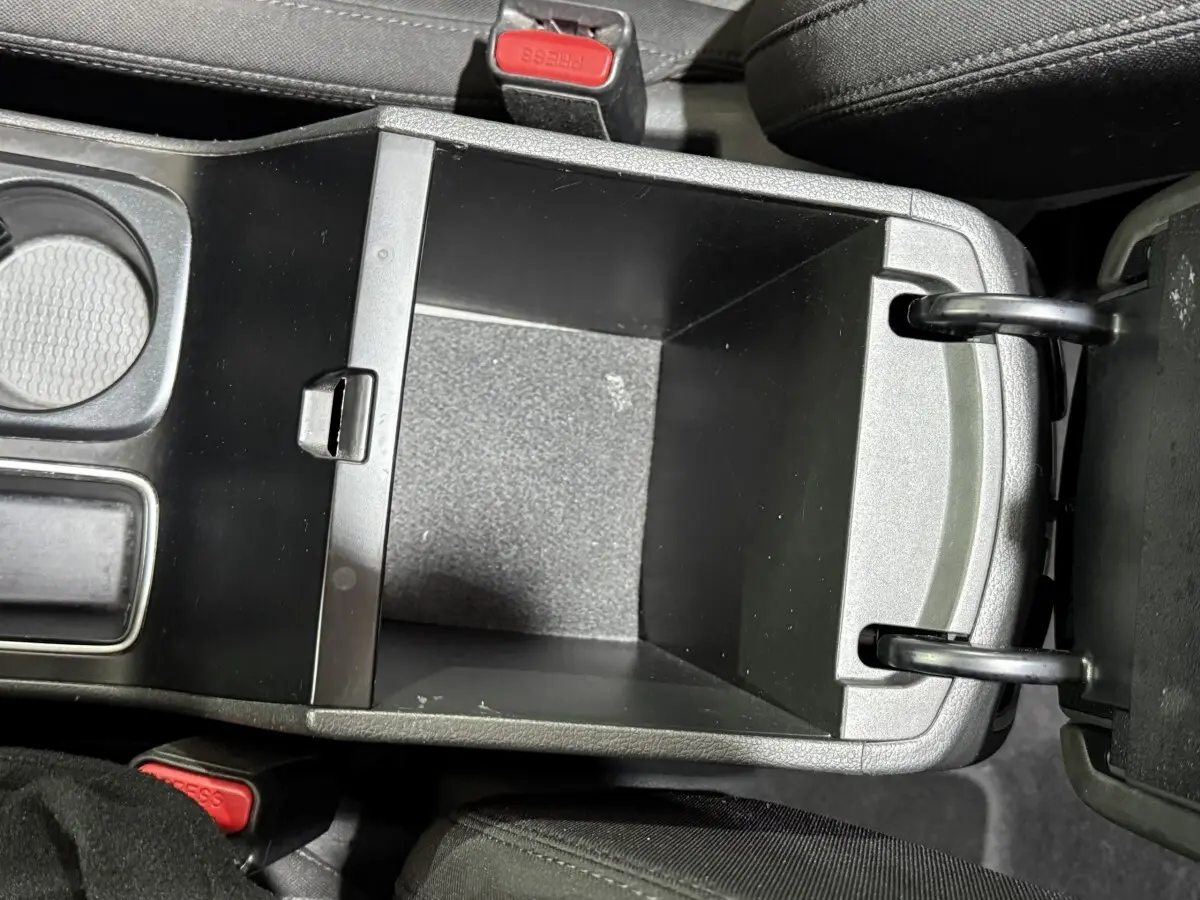 Vue plongeante sur le rangement central ouvert du Hyundai Tucson noir, montrant l'espace intérieur vide et les sièges en tissu noir.