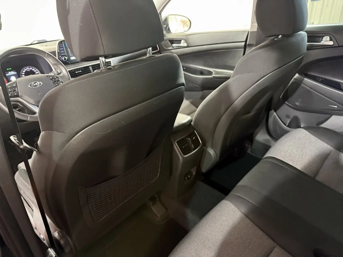 Vue intérieure arrière du Hyundai Tucson 2019 noir, montrant les sièges tissu bicolore et la console centrale avec aérateurs.