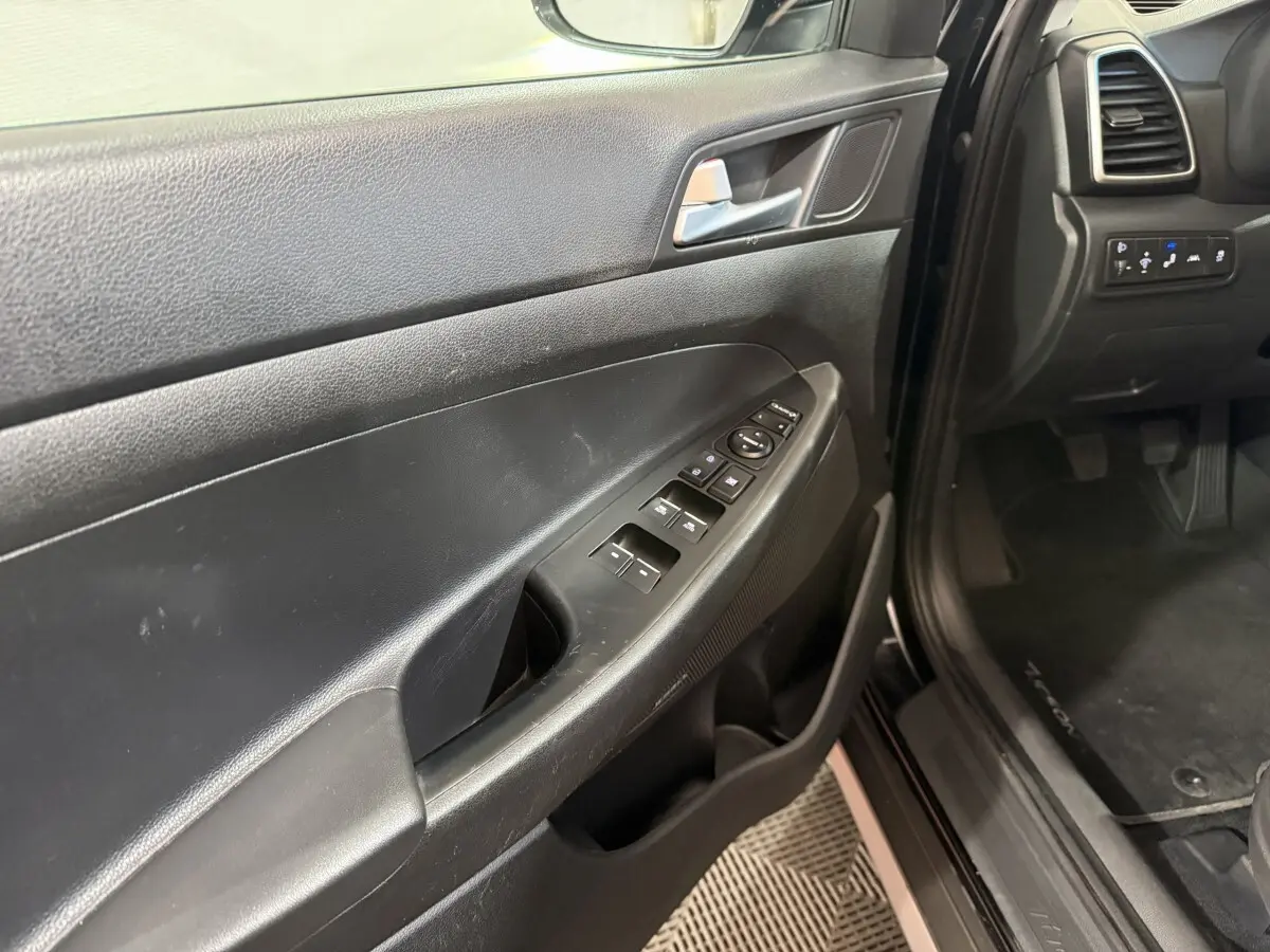 Vue intérieure côté conducteur de la porte noire du Hyundai Tucson 2019 avec commandes électriques des vitres et rétroviseurs.