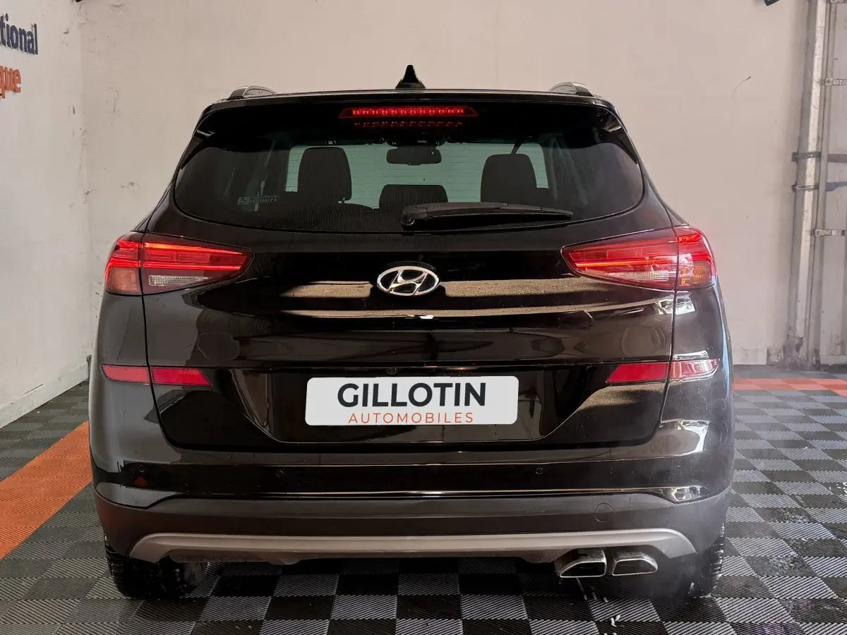 Vue arrière d’un Hyundai Tucson noir 2019 avec feux LED et double sortie d’échappement visible en intérieur showroom.