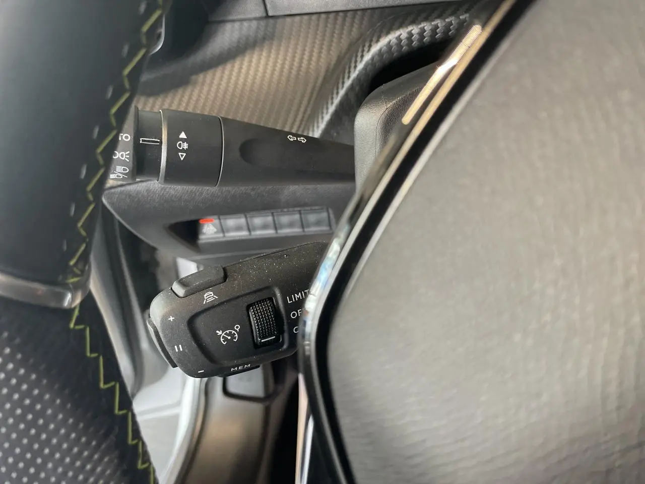 Gros plan sur la commande de régulateur de vitesse à gauche du volant cuir noir sur Peugeot 208 gris clair métallisé.