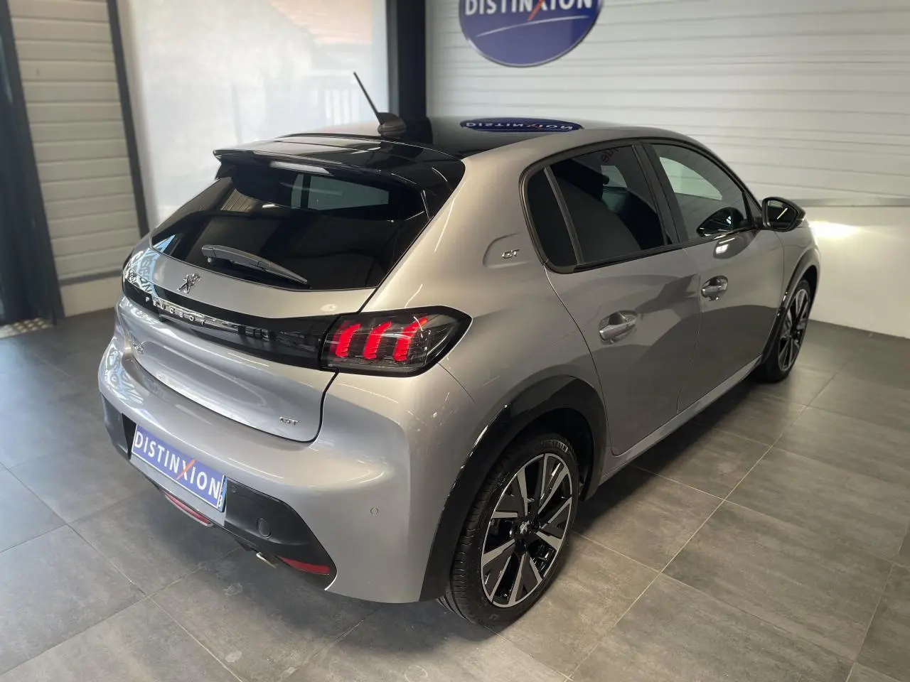 Vue 3/4 arrière droite d'une Peugeot 208 gris clair métallisé avec toit noir et jantes alliage 17 pouces Bronx.