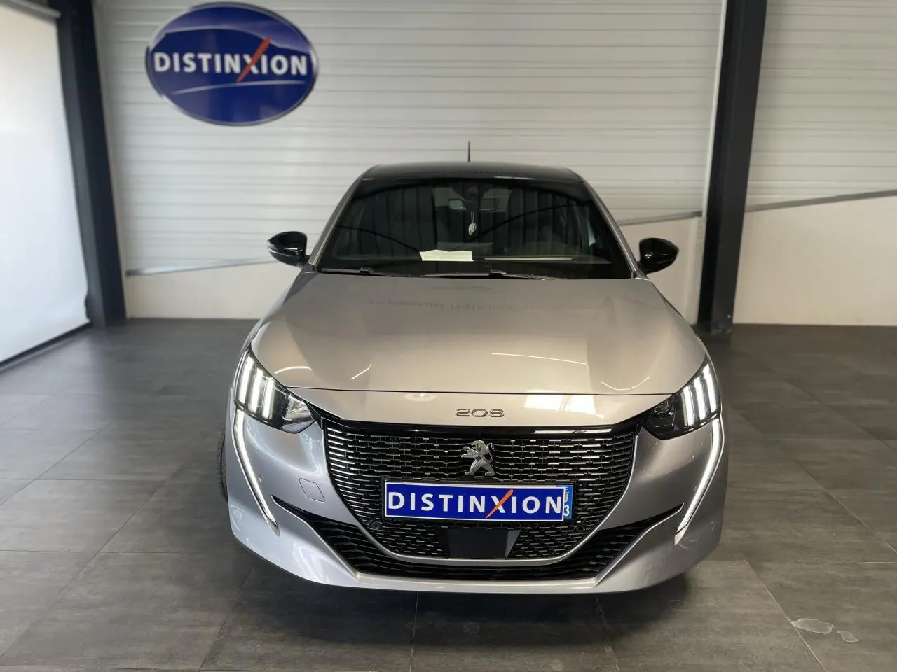 Peugeot 208 gris clair métallisé vue de face en intérieur, avec calandre noire et toit noir brillant.