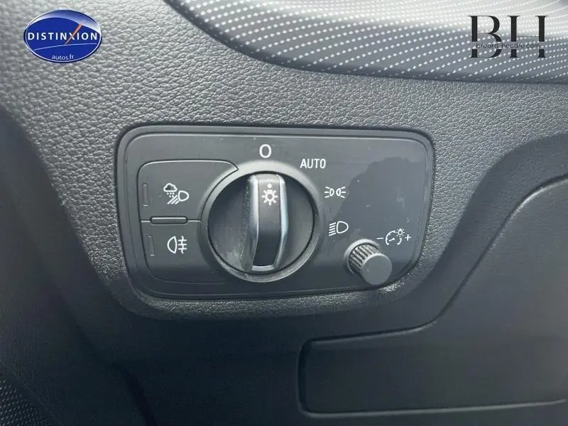 Gros plan sur le sélecteur de phares noir dans l'habitacle de l'Audi Q2 blanc Ibis 2018 côté conducteur.