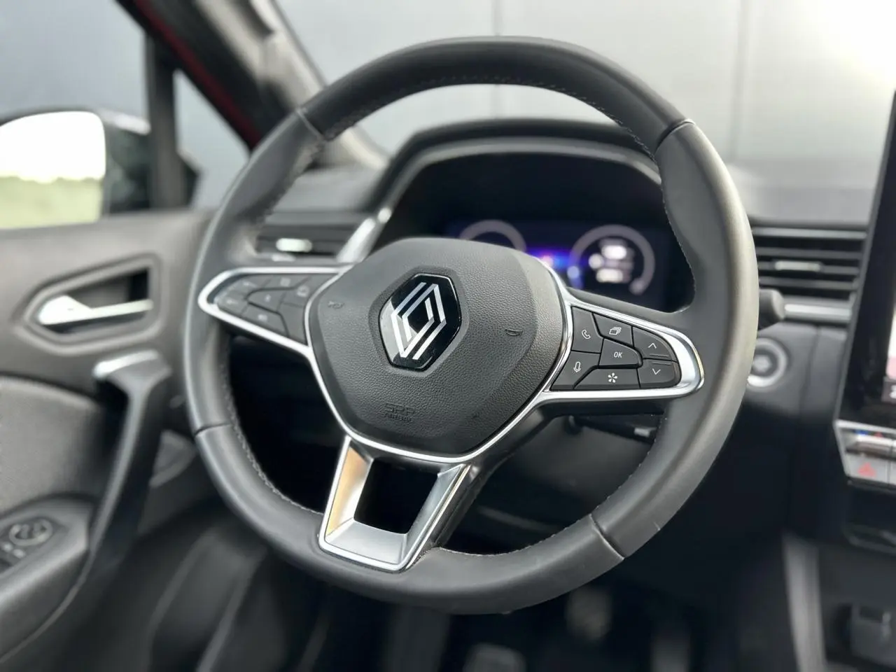 Gros plan sur le volant noir du Renault Captur 2025 avec commandes intégrées et tableau de bord numérique flou.