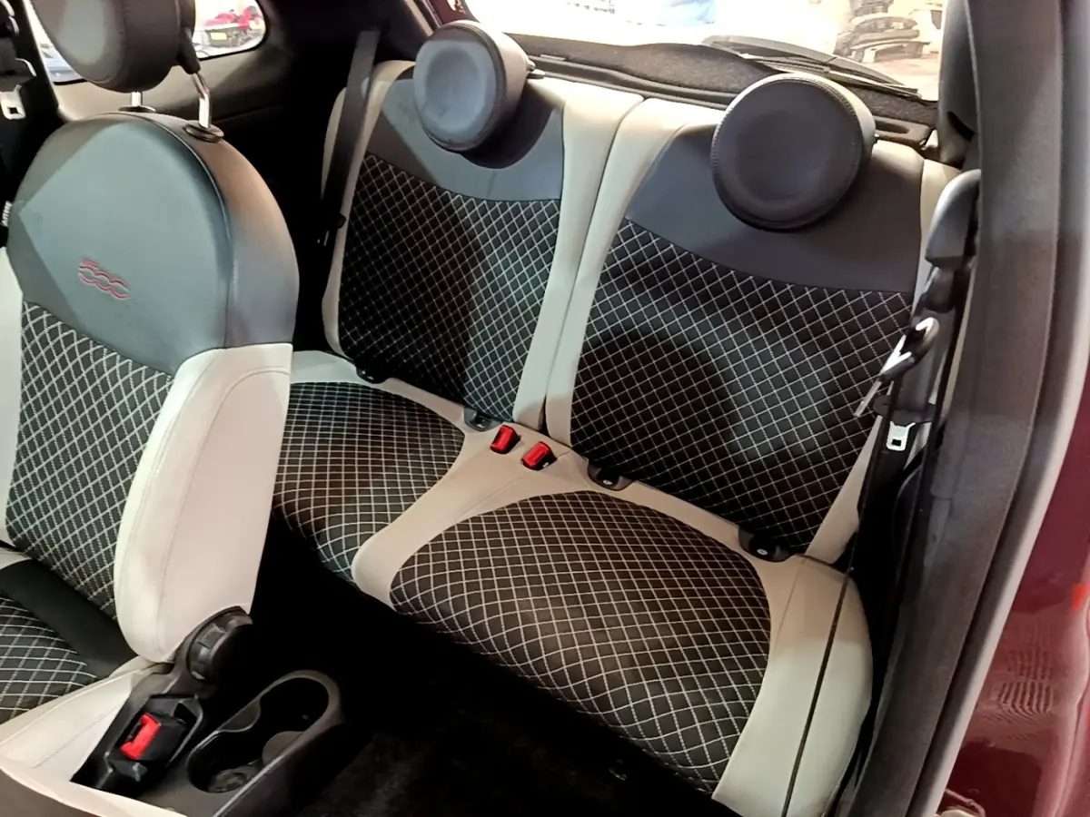 Vue intérieure arrière montrant les sièges arrière en tissu noir à motifs blancs et cuir beige d'une FIAT 500 rouge.