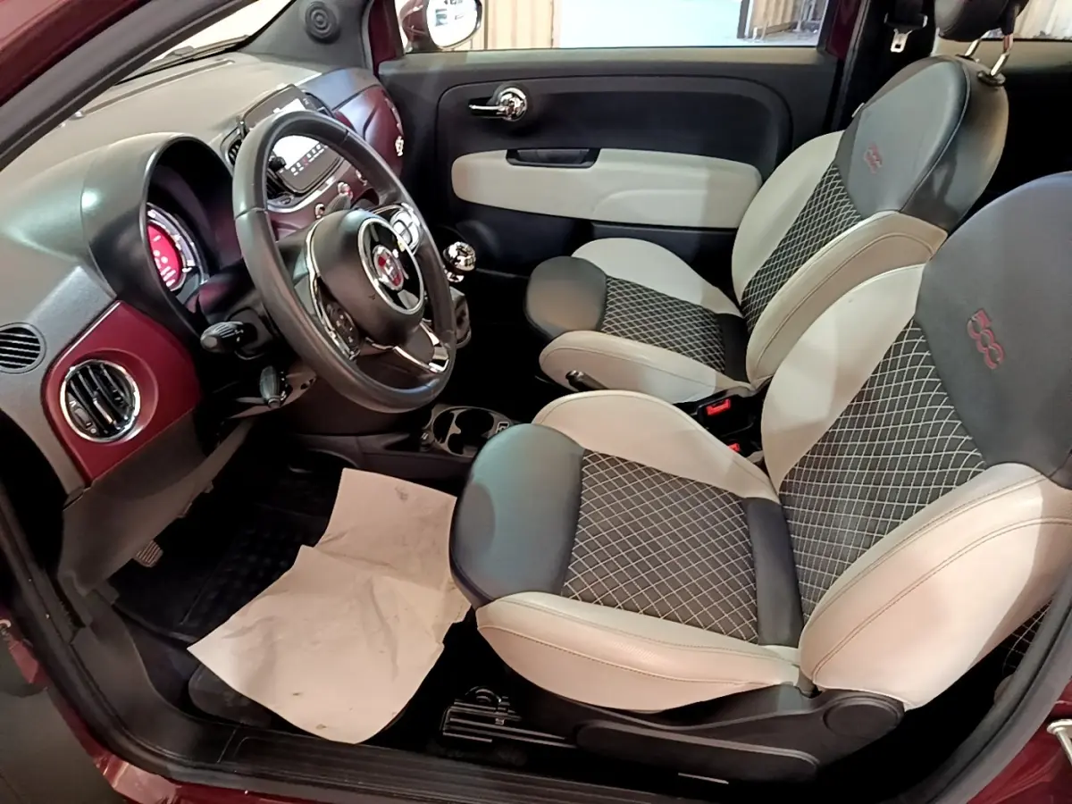 Vue intérieure côté conducteur de la Fiat 500 rouge, avec sièges bi-ton noir et beige et volant cuir multifonctions.