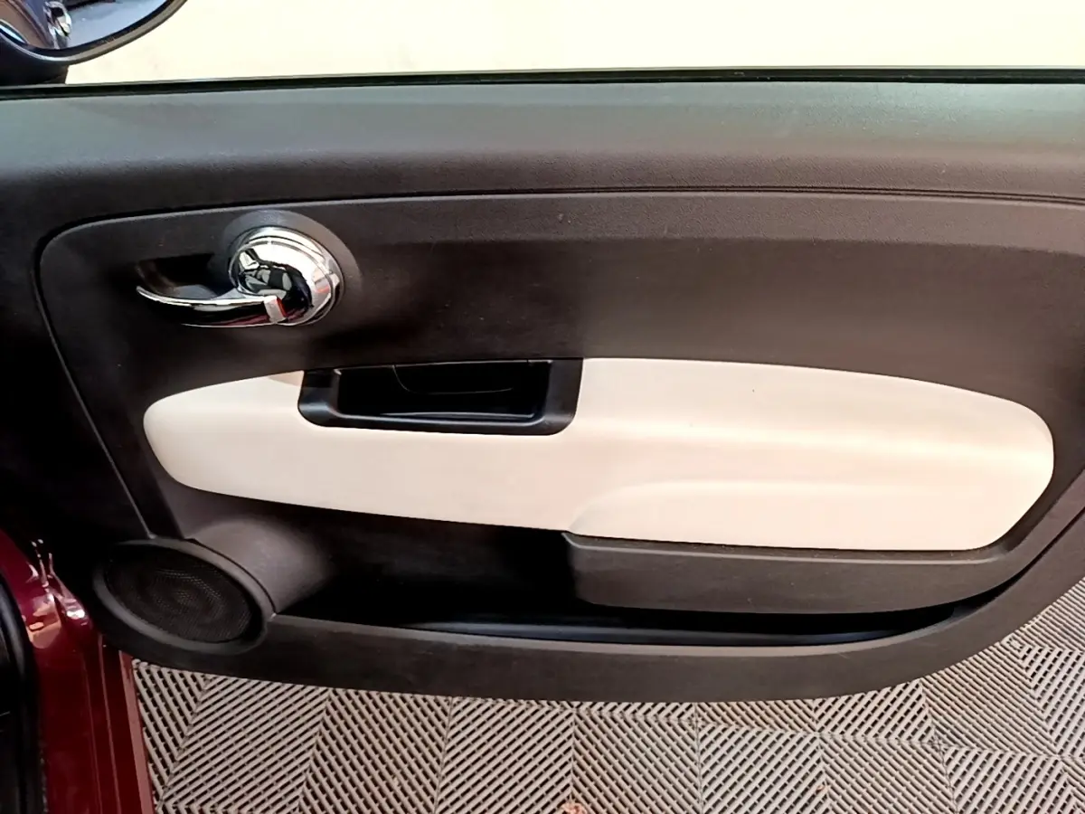 Gros plan sur la porte intérieure côté gauche de la FIAT 500 rouge, avec poignée chromée et insert beige.