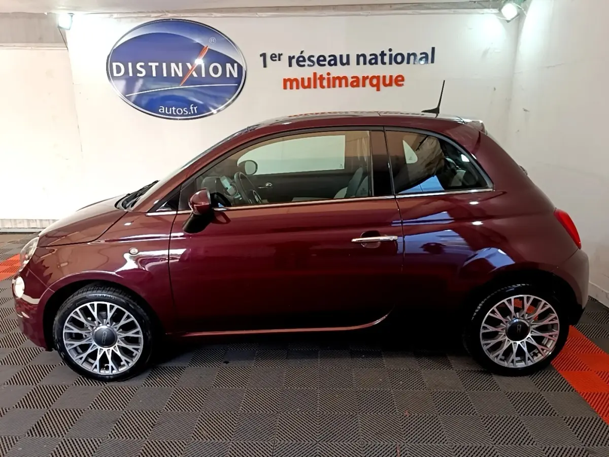 Vue de profil côté gauche d'une FIAT 500 rouge bordeaux 2021 avec jantes alliage et toit noir en intérieur showroom.