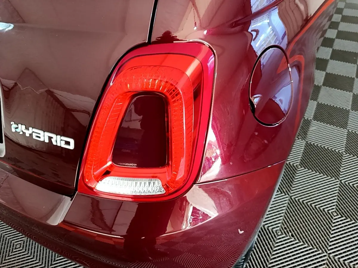 Gros plan sur le feu arrière droit rouge et l’inscription Hybrid d’une FIAT 500 rouge, avec la trappe à carburant visible.