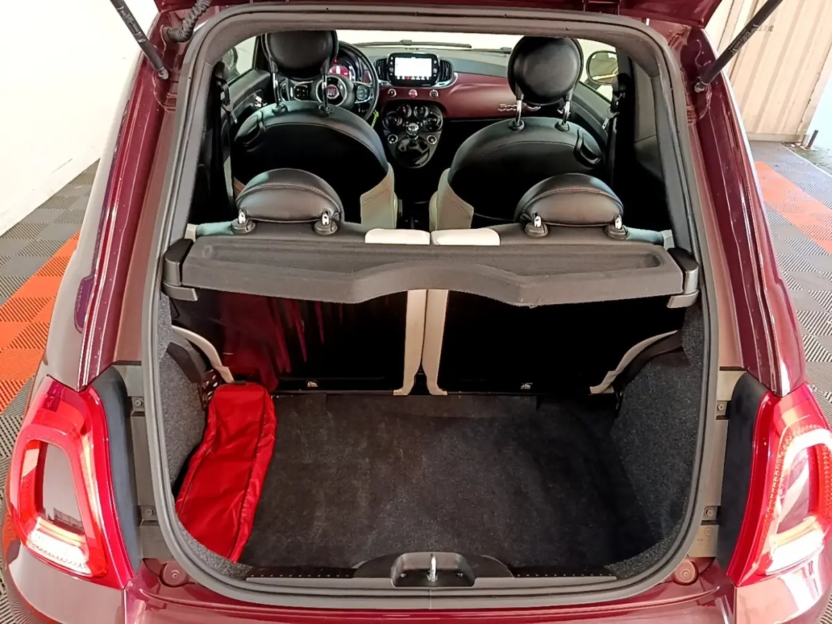 Vue arrière du coffre ouvert d'une FIAT 500 rouge, montrant l'intérieur noir des sièges et le tableau de bord.