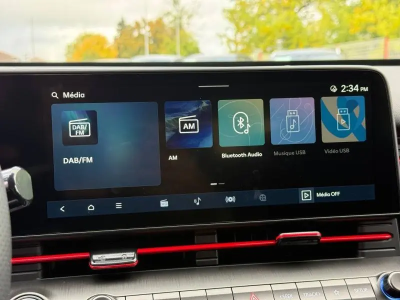 Écran tactile multimédia intérieur de la Hyundai Kona 2025 avec interface audio et bandeau rouge sous la ventilation.