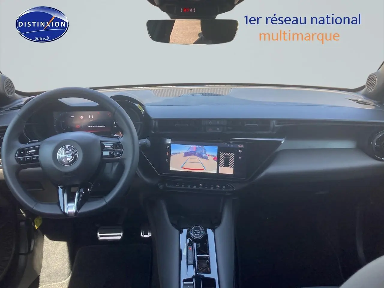 Vue intérieure avant de l'Alfa Romeo Junior 1.2 hybride ivoire et noir, avec tableau de bord numérique et écran tactile affichant la caméra de recul.