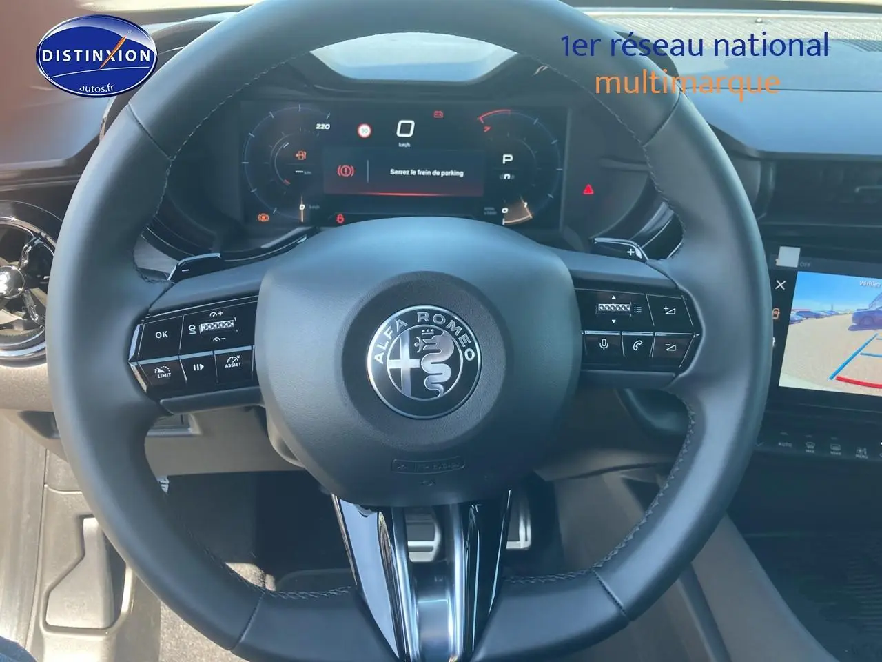 Vue rapprochée du volant noir de l'Alfa Romeo Junior 1.2 hybride avec tableau de bord numérique et écran tactile.