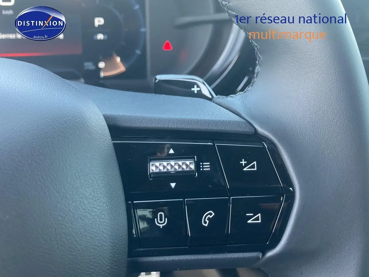 Gros plan sur les commandes au volant à droite de l'Alfa Romeo Junior 1.2 hybride ivoire et noir, avec tableau de bord numérique en arrière-plan.