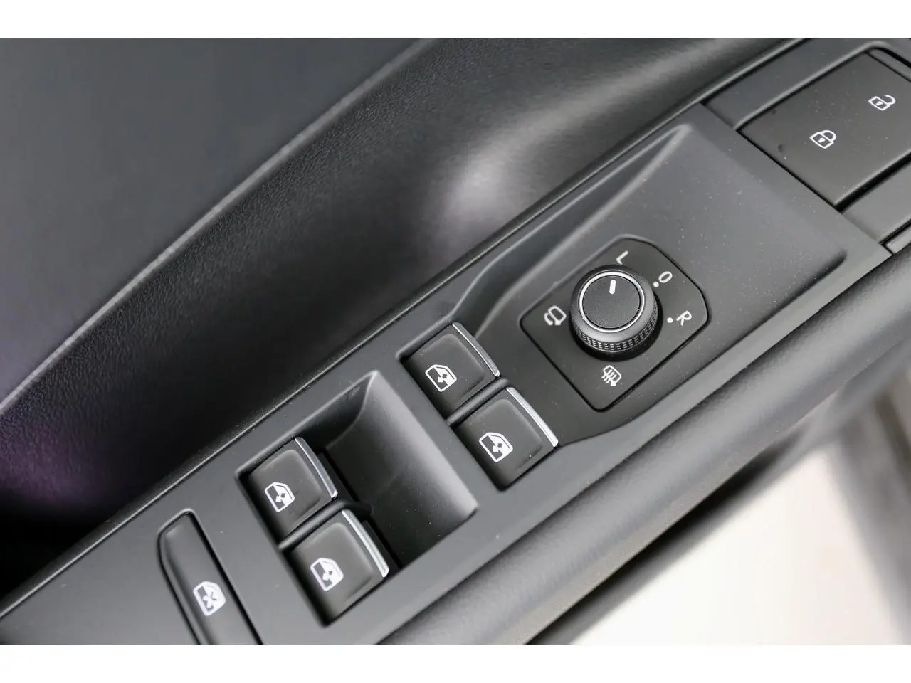 Gros plan sur les commandes de lève-vitres et réglage des rétroviseurs côté conducteur du Volkswagen T-Roc gris.