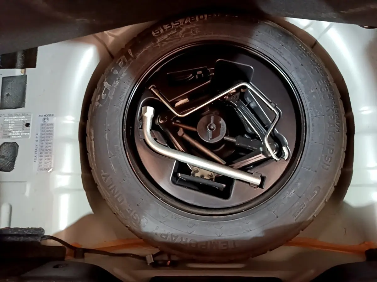Gros plan sur la roue de secours et les outils de bord dans le coffre d'une FIAT 500 gris foncé.