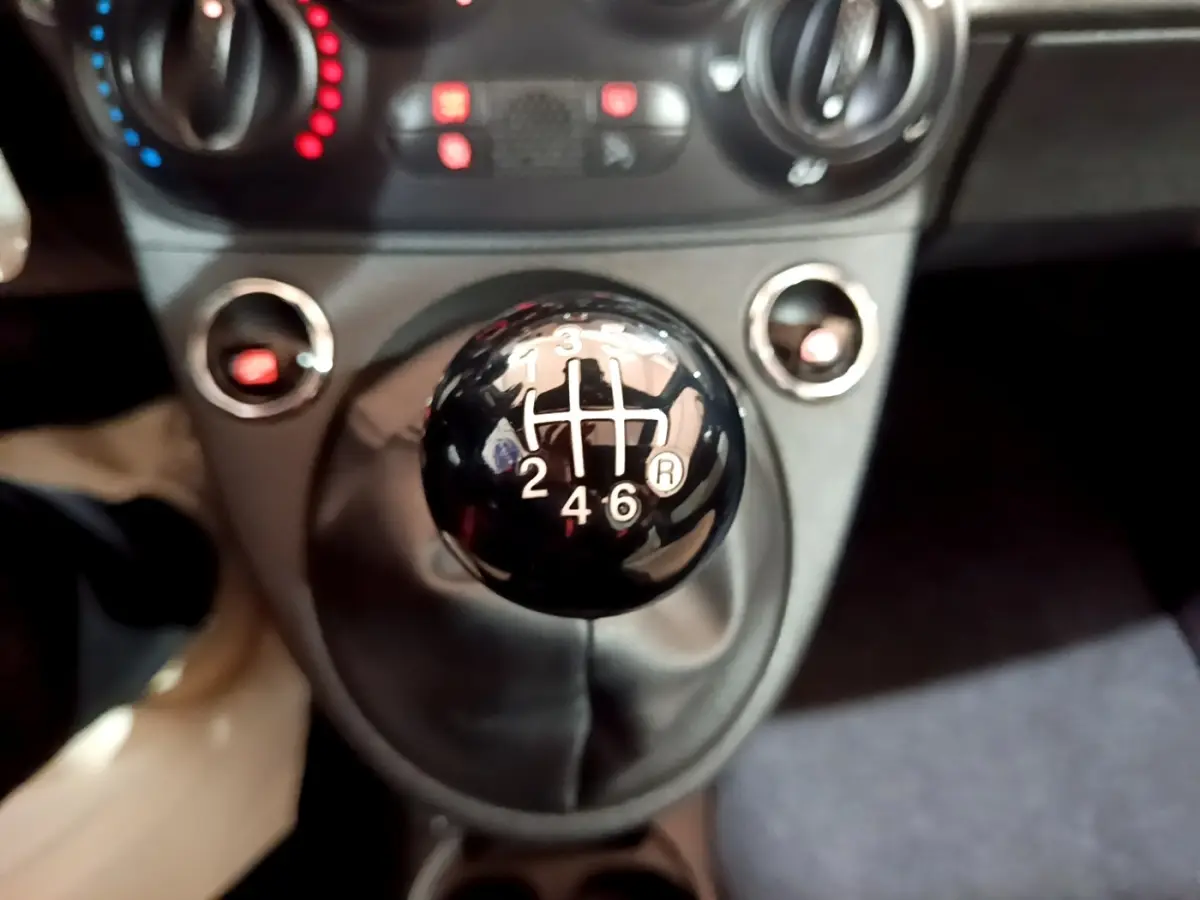 Gros plan sur le levier de vitesse manuel noir de la FIAT 500 Hybrid, avec tableau de bord et commandes en arrière-plan flou.