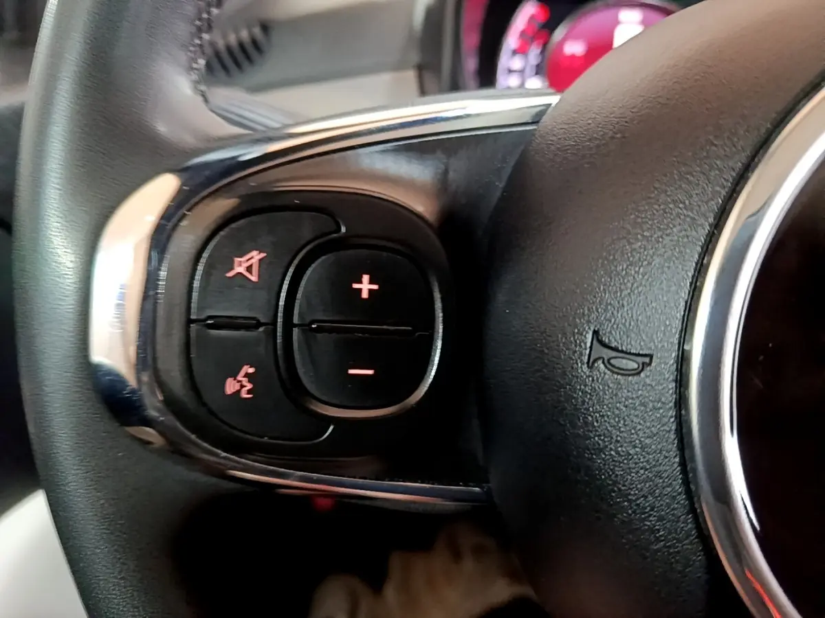 Gros plan sur le volant cuir noir multifonctions du Fiat 500 Hybrid, avec commandes de volume et téléphone intégrées.