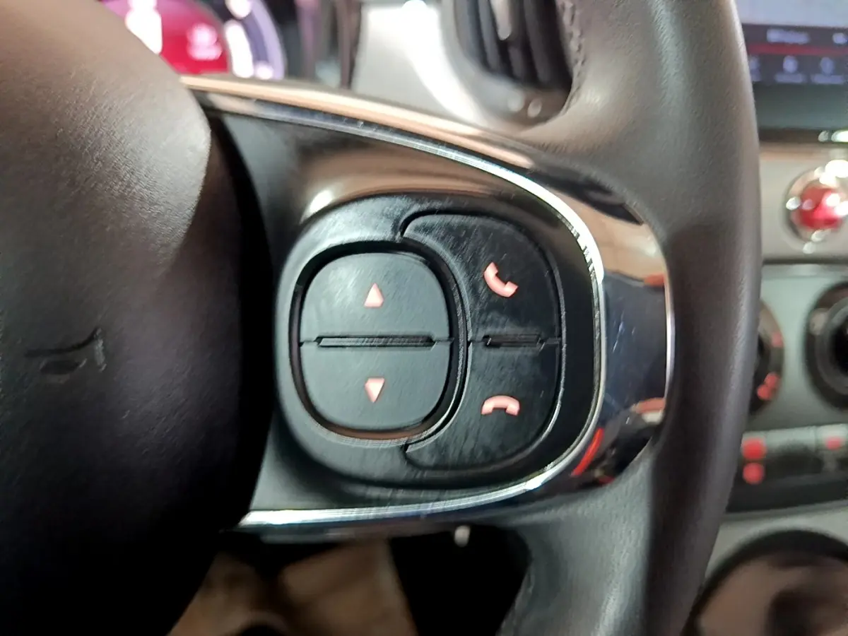 Gros plan sur les commandes du volant cuir noir de la Fiat 500 Hybrid, boutons de gestion d’appels visibles.