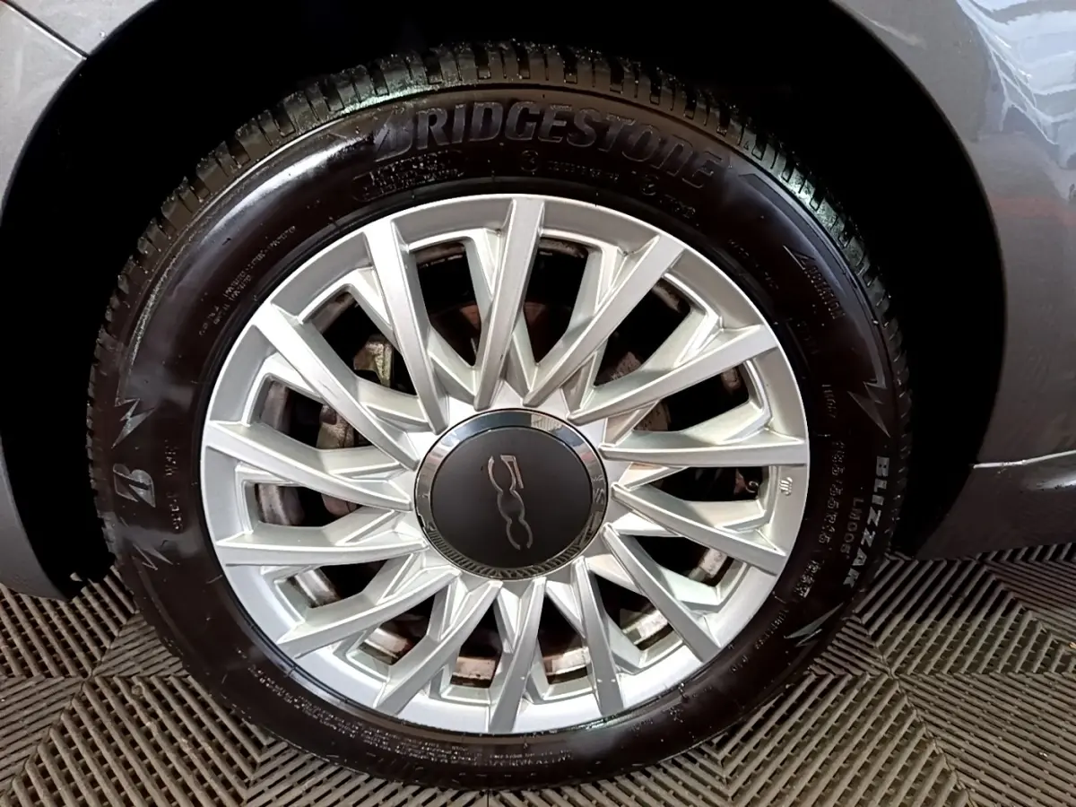 Gros plan sur la jante argentée et le pneu Bridgestone d'une FIAT 500 gris foncé, détail de la roue avant droite.
