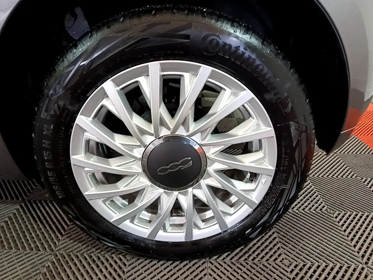Gros plan sur la roue avant droite d'une FIAT 500 gris foncé, avec jante alliage argentée et logo central 500.