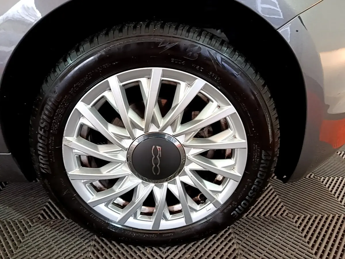 Gros plan sur la roue avant droite d'une FIAT 500 gris foncé avec jante alliage multibranches et logo central.