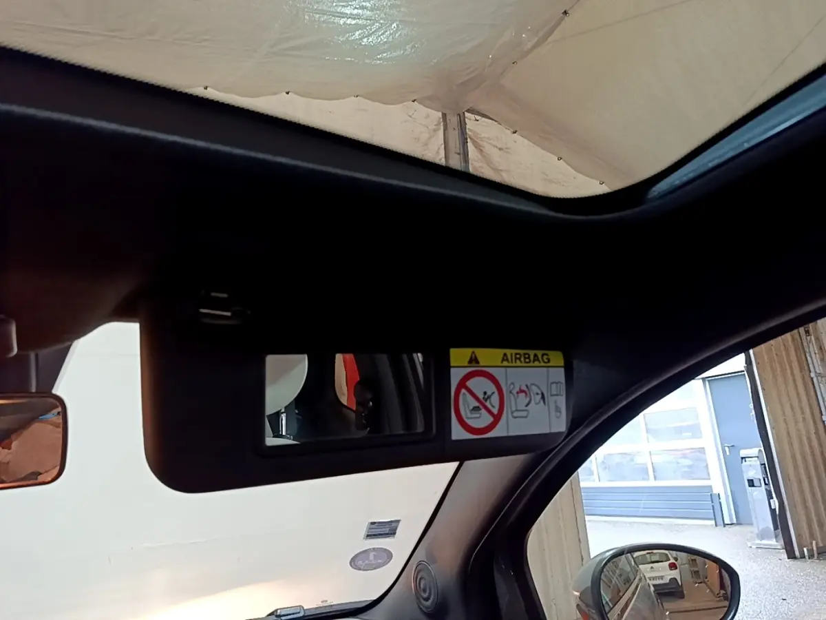 Vue intérieure sur le pare-soleil avec miroir et avertissement airbag, fenêtre ouverte côté droit, Fiat 500 gris foncé visible en reflet.