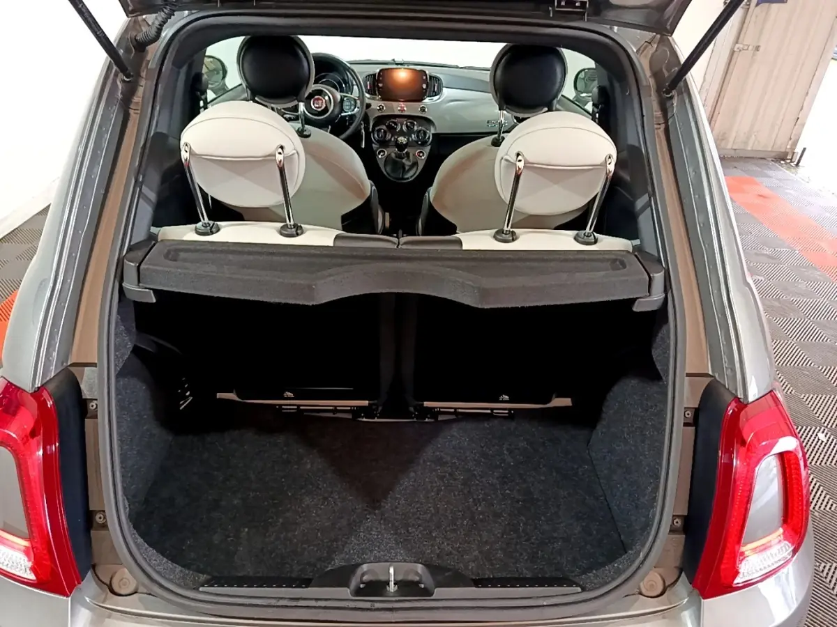 Vue arrière ouverte sur coffre et intérieur clair d'une Fiat 500 gris foncé avec tableau de bord et volant visibles.