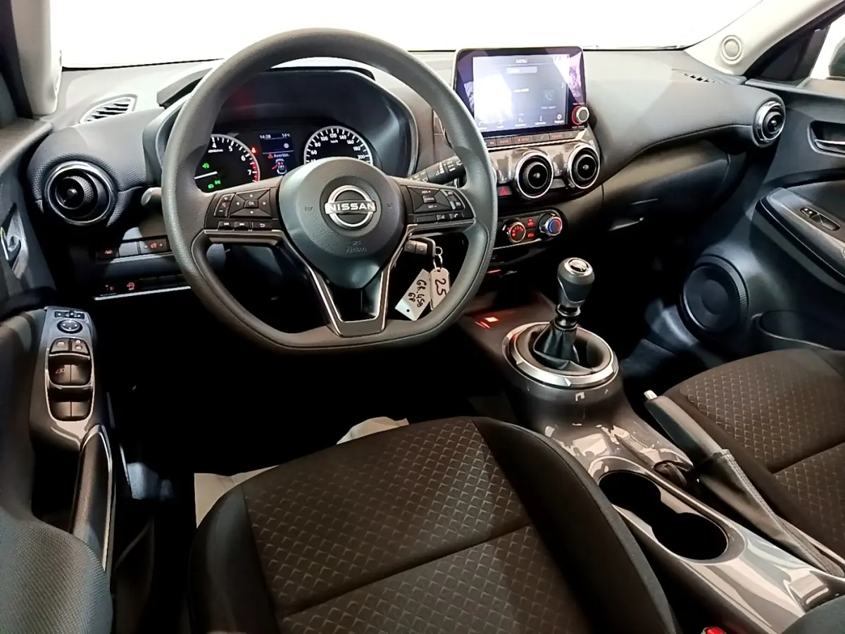 Vue intérieure avant du Nissan Juke noir 2023, volant multifonctions, écran tactile et levier de vitesse manuel visibles.