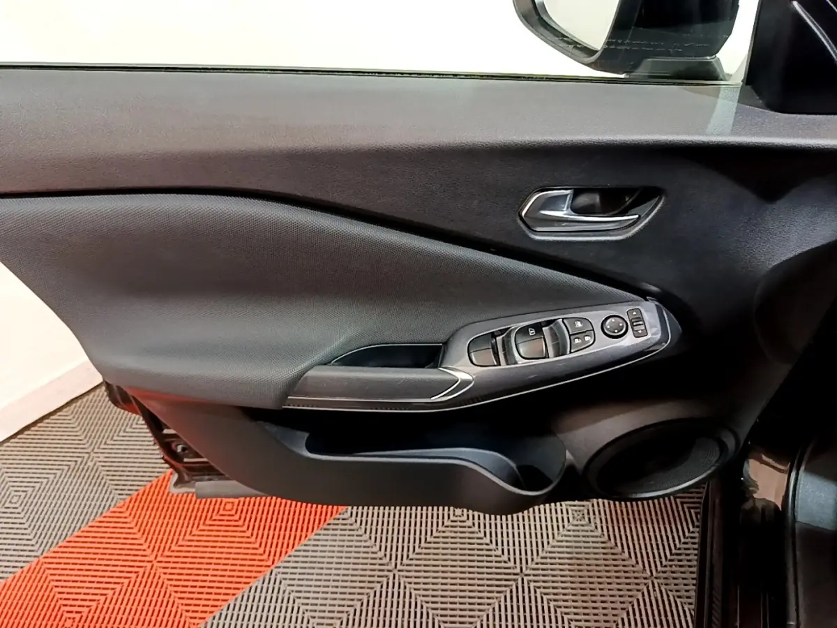 Vue intérieure côté gauche de la porte avant noire du Nissan Juke 2023, avec commandes électriques des vitres et rétroviseur.