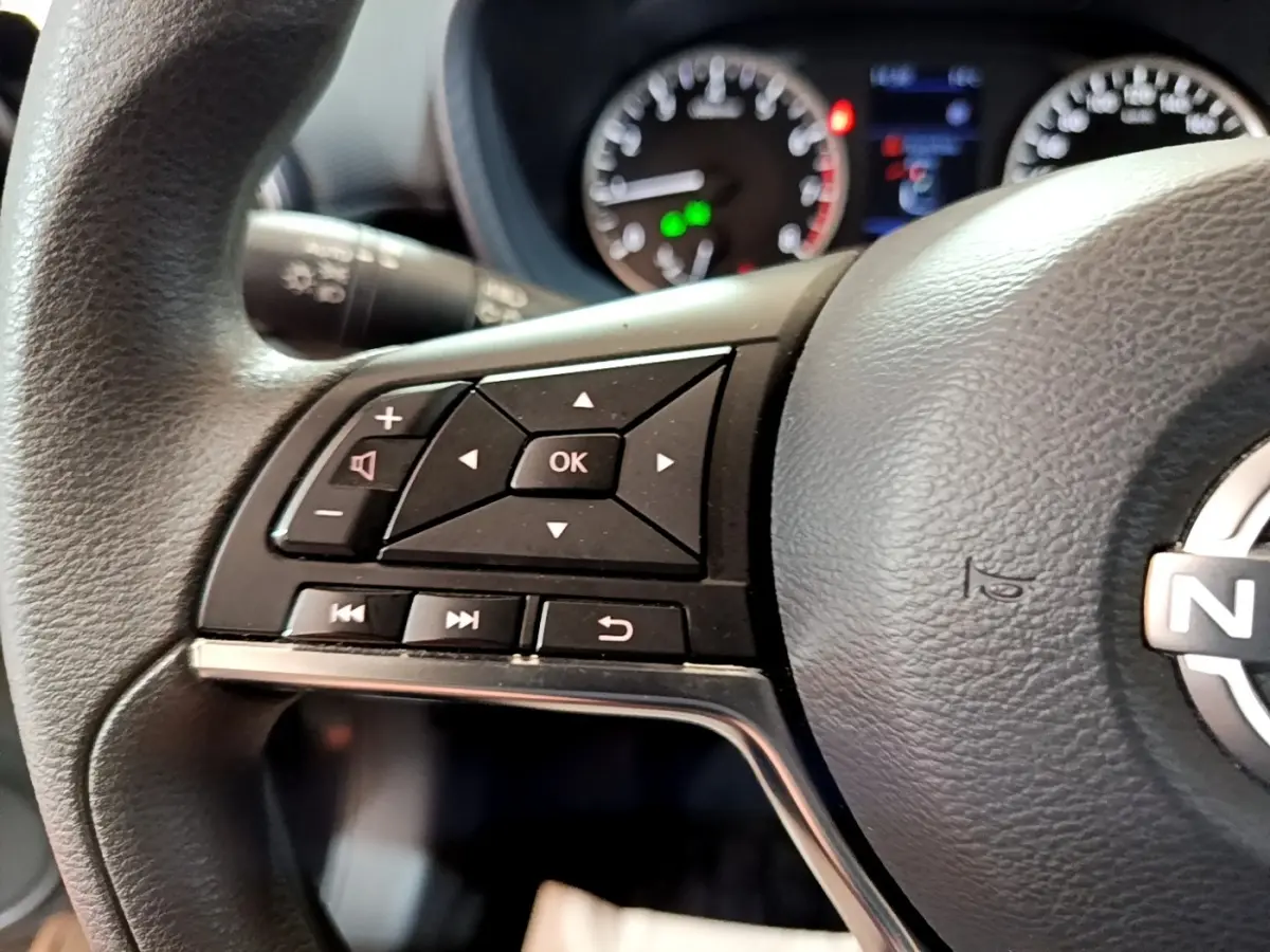 Gros plan sur les commandes multifonctions au volant noir du Nissan Juke 2023 avec tableau de bord et compteurs en arrière-plan flous.