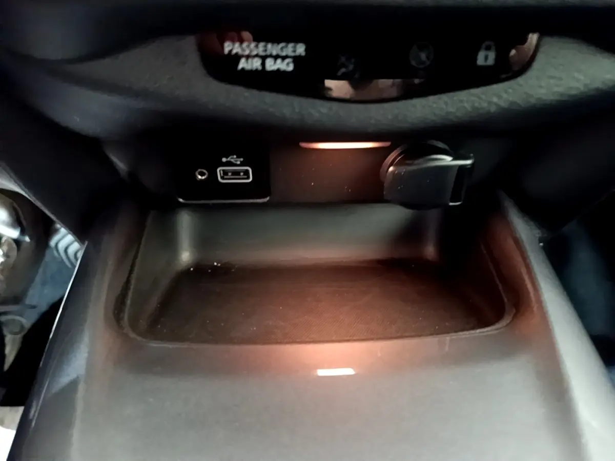 Gros plan sur la console centrale noire du Nissan Juke 2023 avec prise USB et allume-cigare éclairés.