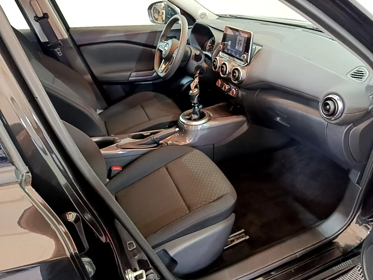 Vue intérieure côté conducteur du Nissan Juke noir 2023, montrant sièges, volant multifonctions et écran tactile central.